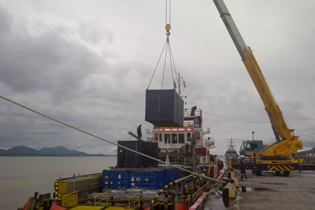 A crawler crane loading a container onto a vessel at a wharf